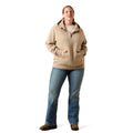 A woman modeling a light tan quarter-zip pullover hoodie with a drawstring hood and kangaroo pockets, paired with blue jeans and brown shoes, against a plain white background.