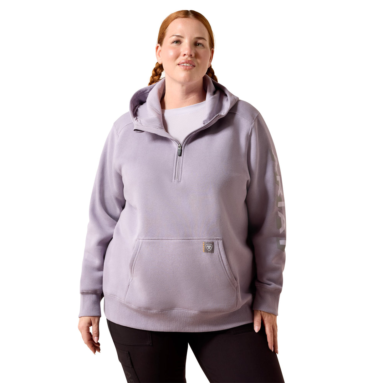 A woman modeling a light lavender half-zip hoodie with a kangaroo pocket and a small logo patch on the pocket, paired with black leggings against a plain white background.