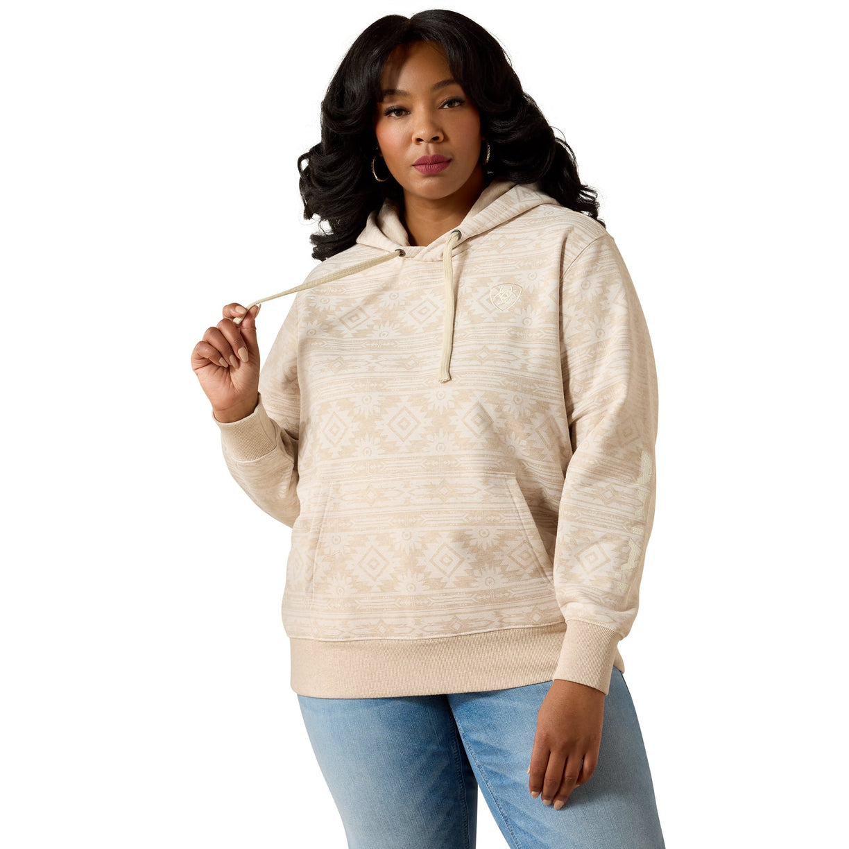 A woman modeling a cream-colored patterned hoodie with drawstrings and a front kangaroo pocket, paired with light blue jeans, against a solid white background.