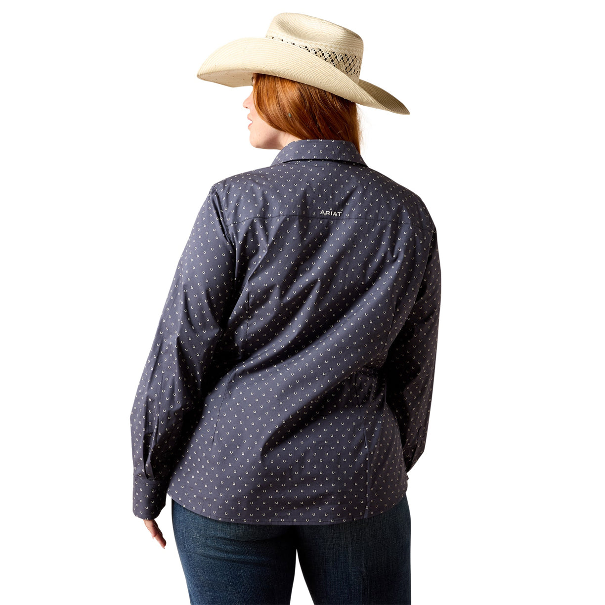 A woman shown from the back wearing a dark navy long-sleeve button-up shirt with a small white polka dot pattern, paired with a beige cowboy hat and dark jeans, against a solid white background.