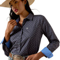 A woman wearing a dark navy western-style button-up shirt with a small repeating white monogram pattern, bright blue turned-back cuffs, and a cowboy hat, photographed against a clean white background.