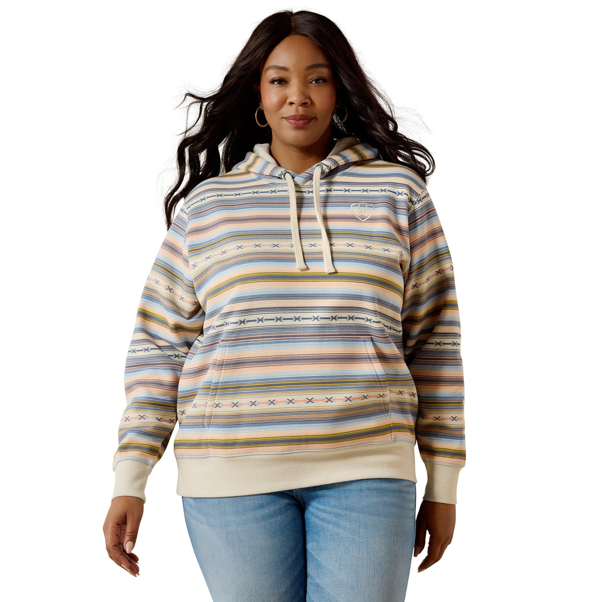 A woman modeling a striped pullover hoodie with a multicolor pattern of beige, blue, yellow, and brown horizontal stripes, paired with light blue jeans against a plain white background.