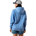 A woman shown from the back wearing a light blue heathered pullover hoodie, denim shorts, and a gray and navy trucker cap against a plain white background.