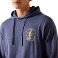 A close-up of a person wearing a heathered navy blue hoodie with a distressed gold graphic on the left chest that reads 'WILD AS HELL' with a cowboy riding a horse.