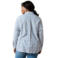 A woman viewed from the back wearing a light blue and white patterned button-up shirt and blue jeans against a plain white background.