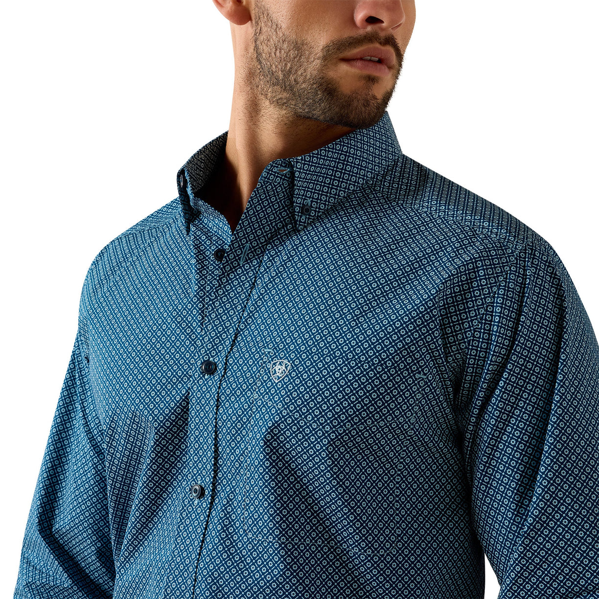 A close-up of a man wearing a blue patterned button-down shirt against a plain white background.
