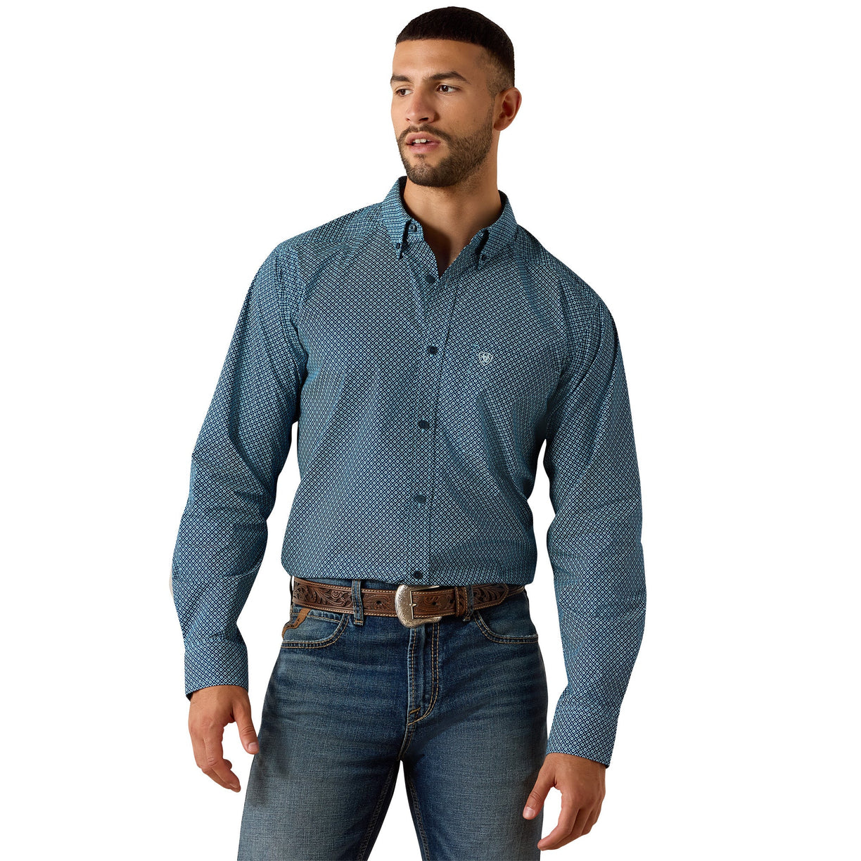 A man wearing a blue long-sleeve button-down shirt with a small white geometric pattern, paired with blue jeans and a brown belt, against a plain white background.