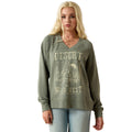 A blonde woman modeling an olive green long-sleeve V-neck sweatshirt with a distressed beige 'Desert Wild West' graphic on the front, paired with light blue jeans against a plain white background.