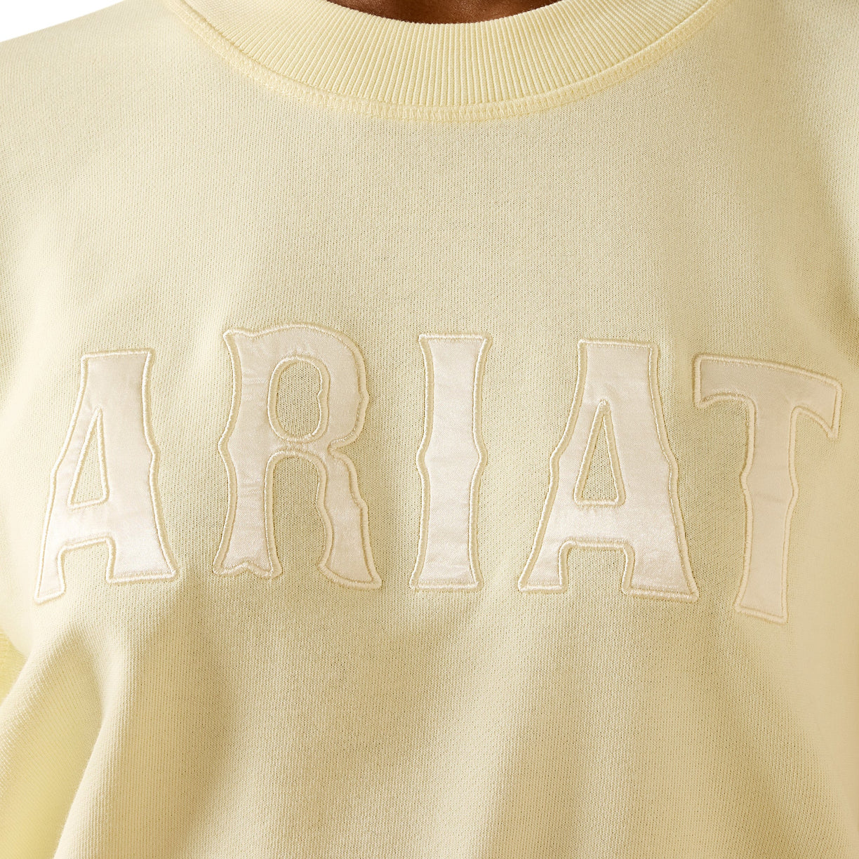 Light yellow sweater with 'ARIAT' branding on a close-up view