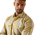 A man wearing a yellow and beige plaid button-down shirt, shown from the chest up against a plain white background.