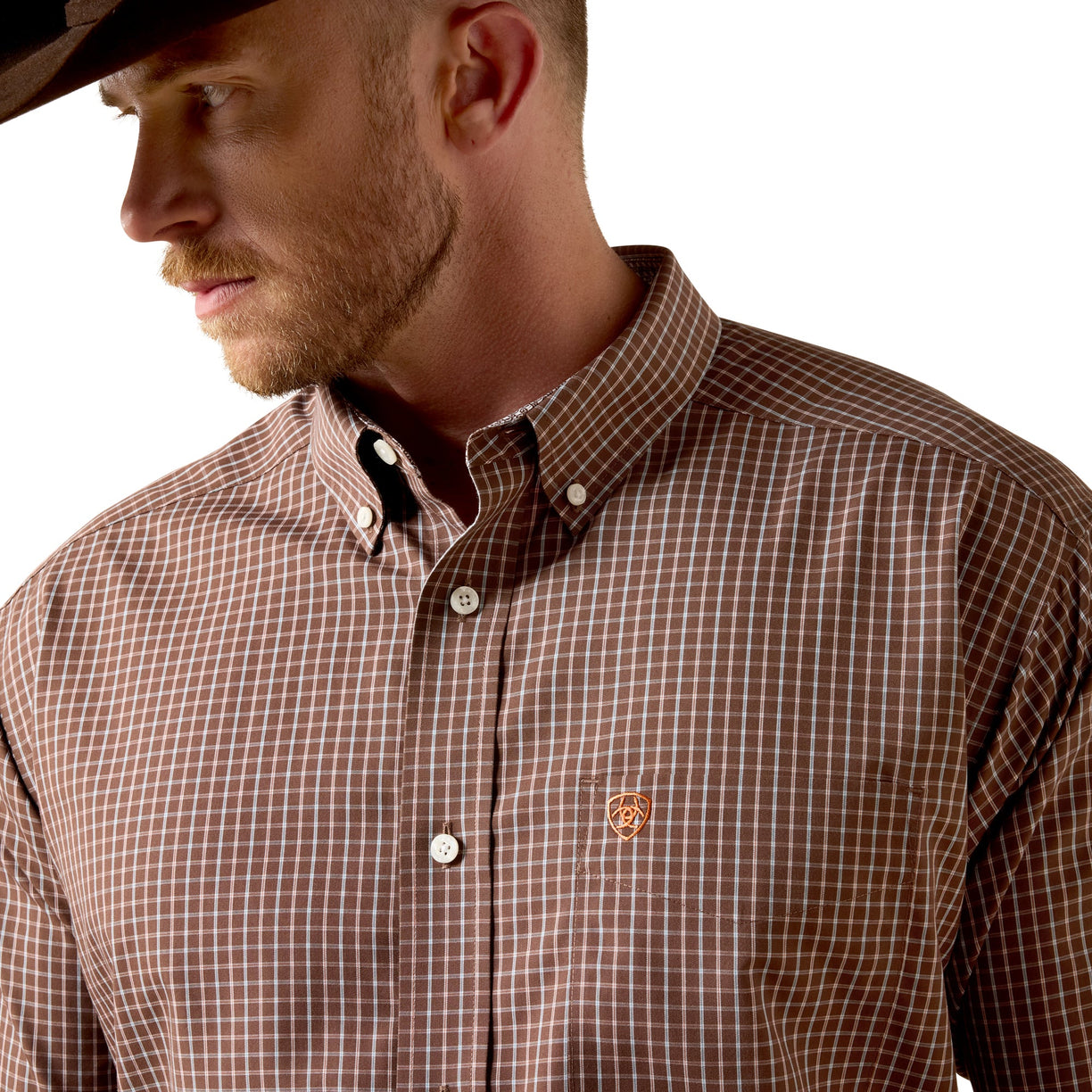 A man wearing a brown and white checkered button-down shirt with a small embroidered logo on the chest, paired with a black cowboy hat against a white background.