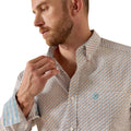 A close-up of a man wearing a light beige button-down shirt with a small blue geometric pattern, adjusting the collar against a white background.