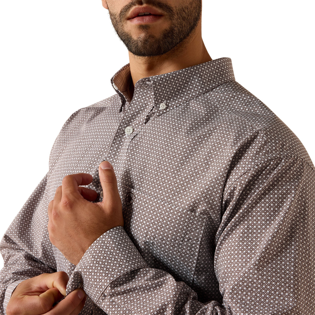 A close-up of a man wearing a brown long-sleeve button-down shirt with a small white geometric pattern, adjusting the cuff with one hand.