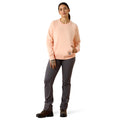 A woman modeling a light peach crewneck sweatshirt and dark gray pants against a plain white background.