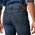 Person wearing blue jeans with Ariat branding on a white background