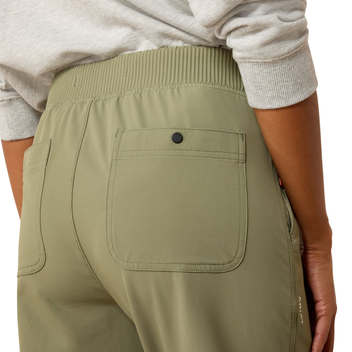 Person wearing olive green pants with a pocket detail on a plain background
