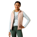Woman wearing a light pink vest over a light blue long-sleeve shirt and green pants on a white background