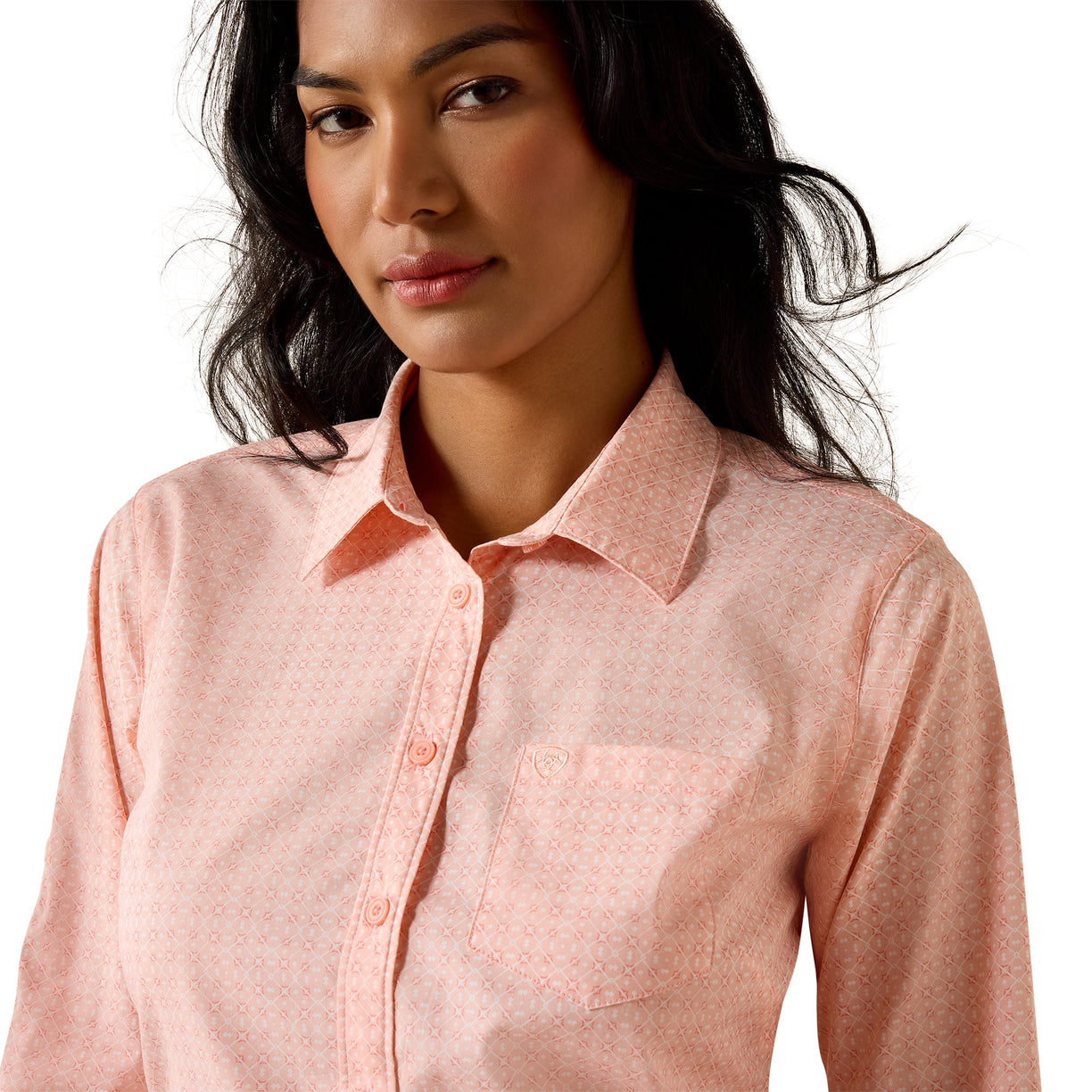 A woman wearing a light pink long-sleeve button-up shirt with a subtle geometric pattern, photographed against a clean white background.