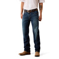 A man wearing dark blue Ariat denim jeans, a brown leather belt, a white button-down shirt, and brown suede boots, shown from the waist down on a white studio background.