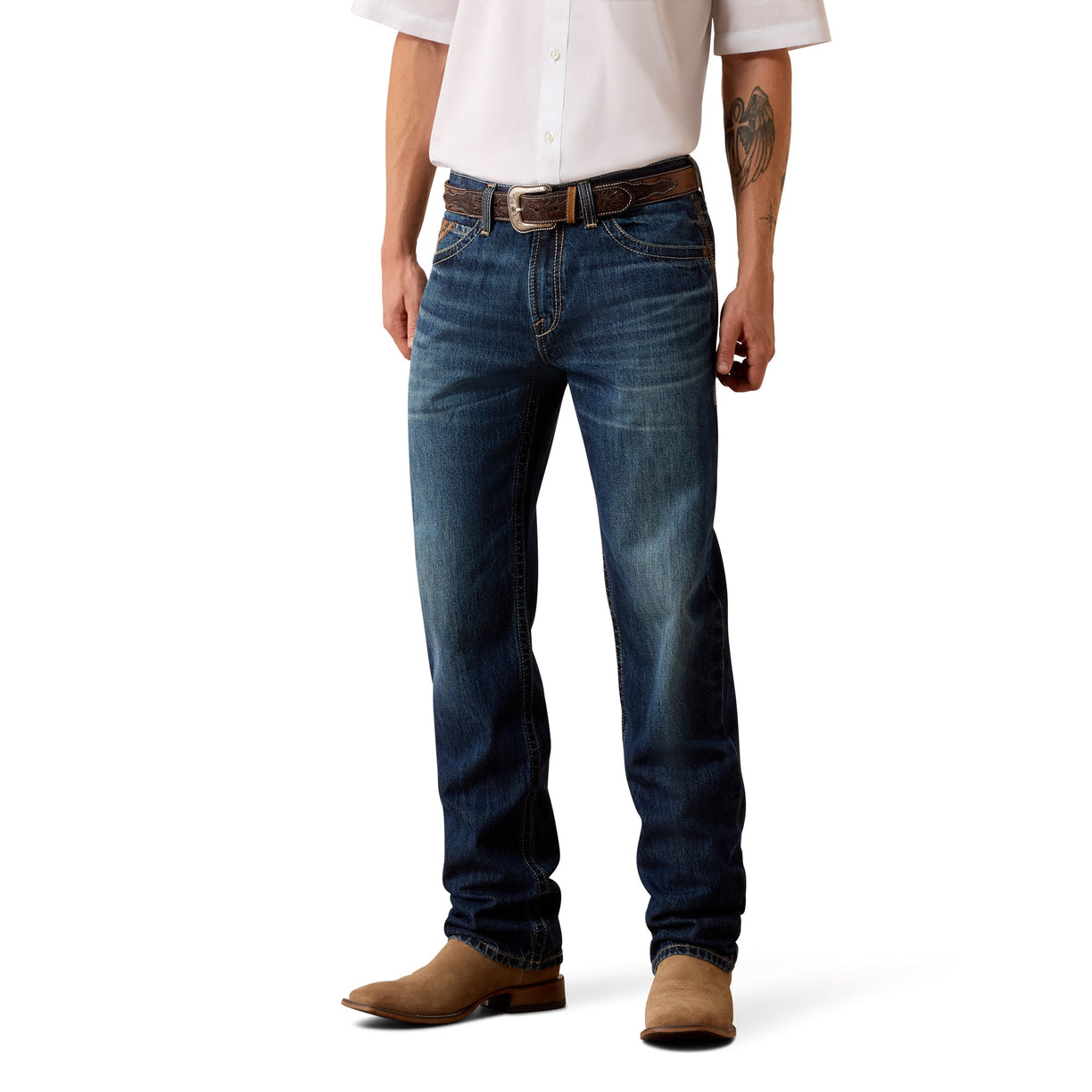 A man wearing dark blue Ariat denim jeans, a brown leather belt, a white button-down shirt, and brown suede boots, shown from the waist down on a white studio background.