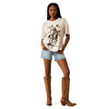 Woman wearing a graphic t-shirt, denim shorts, and brown knee-high boots on a white background