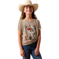 A young girl wearing a beige graphic t-shirt with a desert-themed print, blue jeans, and a cream cowboy hat