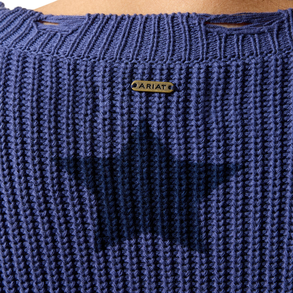 Close-up of a blue knitted garment with 'Ariat' branding on a wooden surface.