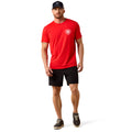 Man wearing a red t-shirt with a logo and black shorts on a white background