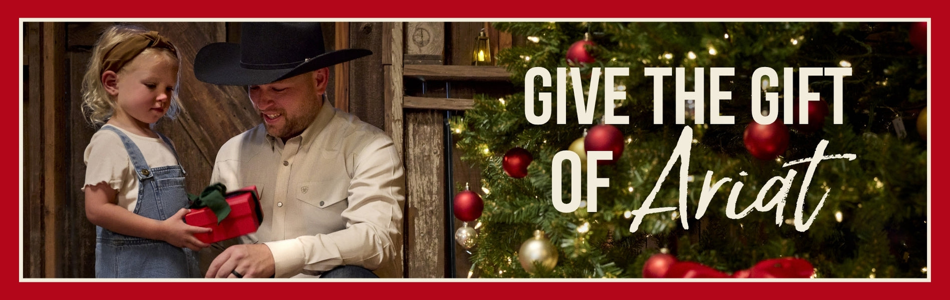 Cowboy giving his daughter a Christmas present in a western barn setting in front of Christmas tree.