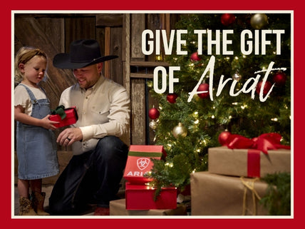 Cowboy giving his daughter a Christmas present in a western barn setting in front of Christmas tree.