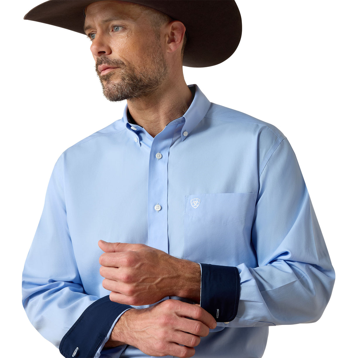 Man wearing a light blue button-up shirt with rolled-up sleeves and a brown cowboy hat on a white background