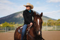 Woman in a cowboy hat riding a horse with mountains in the background