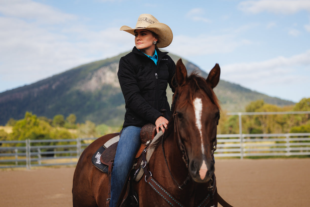 Woman in a cowboy hat riding a horse with mountains in the background