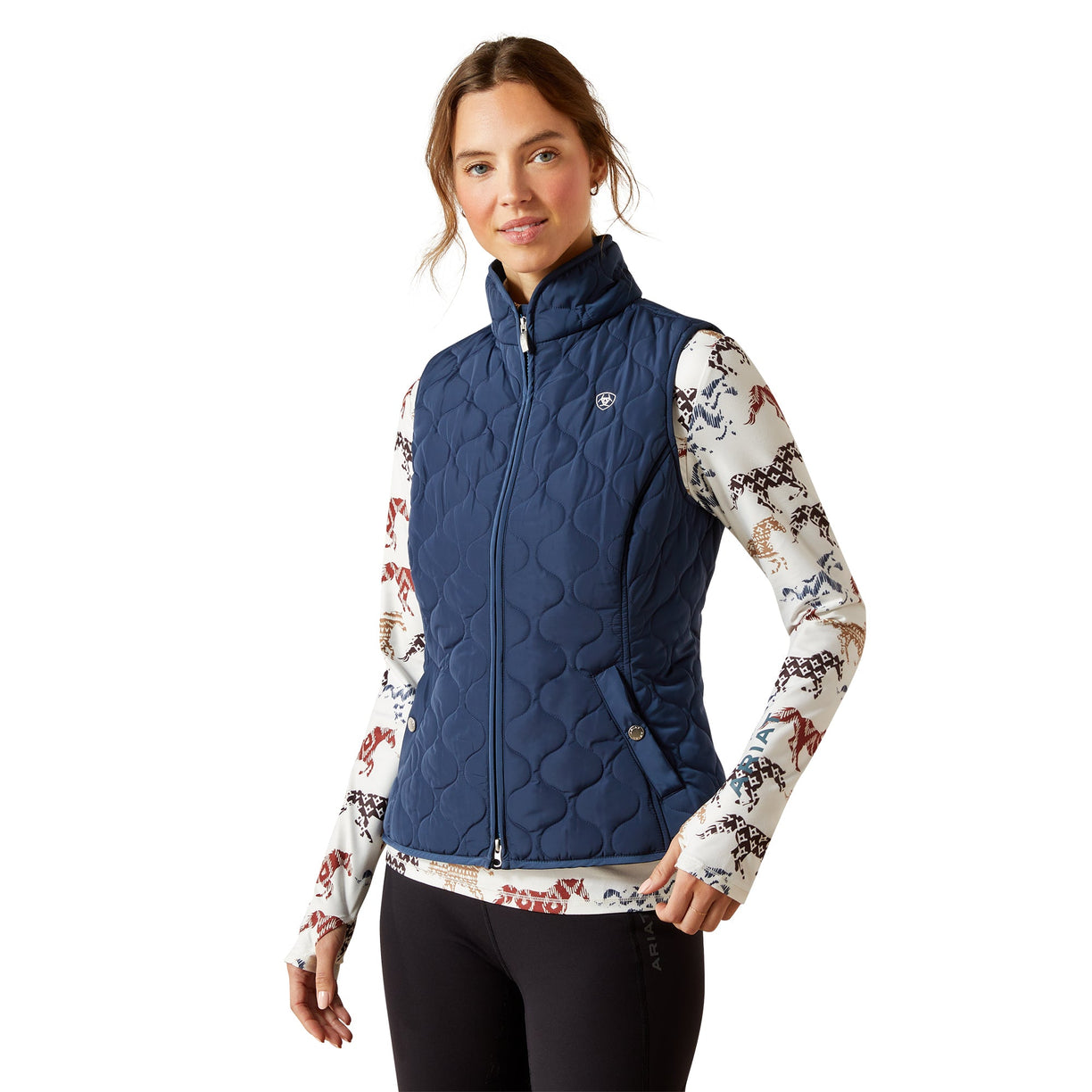 Woman wearing a blue quilted vest over a patterned shirt on a white background