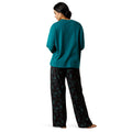 Woman wearing a teal top and black patterned pants on a white background