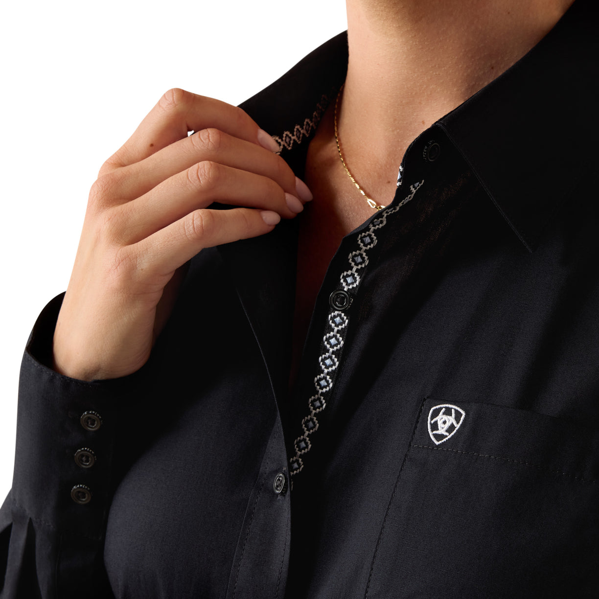 Close-up of a person wearing a dark blue shirt with intricate embroidery and a logo on a white background