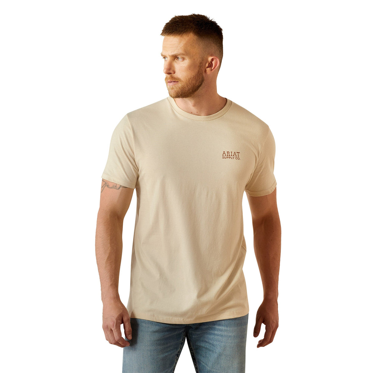 Man wearing a beige t-shirt with 'Ariat Supply' logo on the back, standing against a white background.