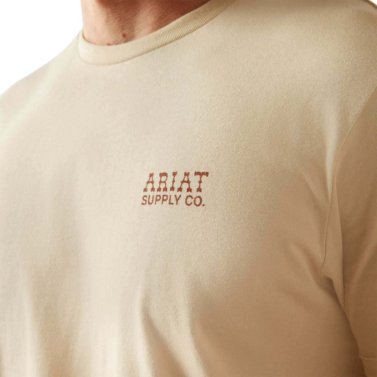 Man wearing a beige t-shirt with 'Ariat Supply' logo on the back, standing against a white background.