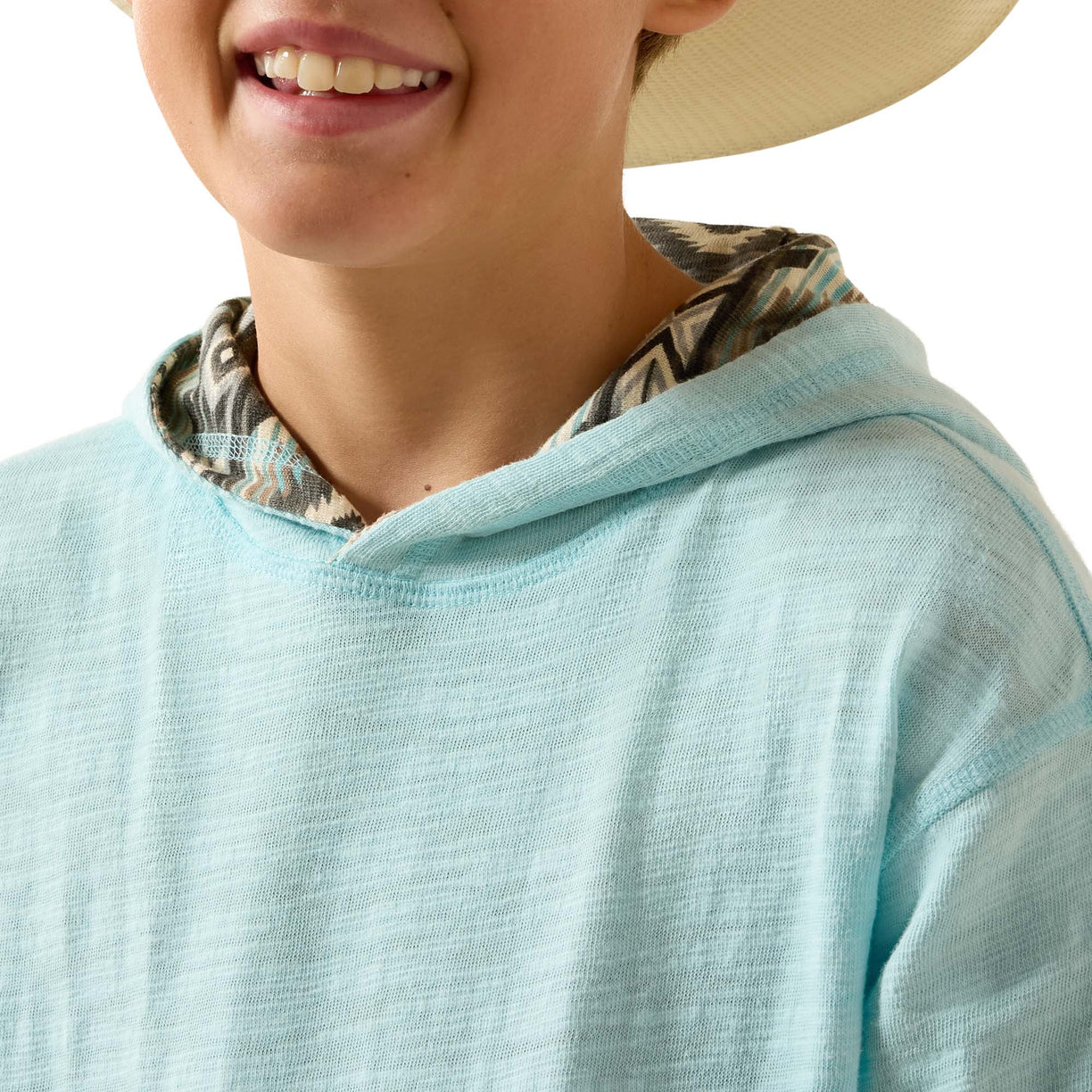 Close-up of a person wearing a light aqua hooded top with a patterned inner hood lining and a beige hat against a white background.