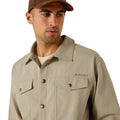 Man wearing a beige Ariat jacket and brown cap on a white background