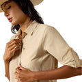 A woman wearing a light beige short-sleeve collared shirt with rolled sleeves and a matching straw hat, shown against a plain white background.