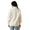 A woman viewed from the back wearing a cream-colored mock neck sweatshirt and light blue jeans against a plain white background.