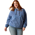 A woman modeling a dusty blue hooded sweatshirt with a subtle white snowflake pattern, paired with light-wash blue jeans against a solid white background.
