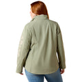A woman with red hair is shown from the back wearing an olive green softshell jacket with a vertical light-colored 'AIPAT' logo on the left sleeve, paired with blue jeans against a white background.