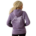A woman with blonde braided hair is shown from the back wearing a lavender-purple hoodie with a white graphic print that reads 'Ariat Premium Quality Estd 1993'.