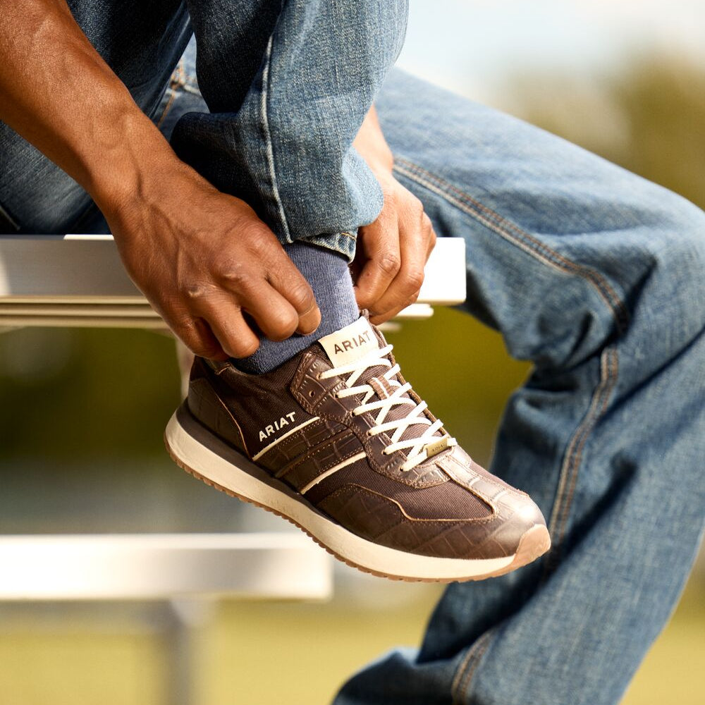 Person tying brown sneakers on a blurred outdoor background