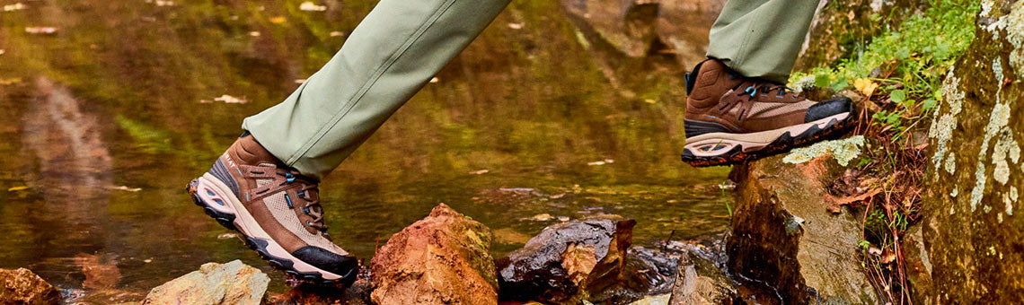 Hiker crossing a creek wearing Ariat Traverse Hiking boots and pants
