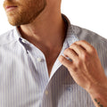 Man adjusting the collar of a striped shirt with a visible brand logo.