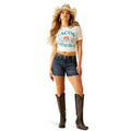 Woman wearing a white t-shirt with text, denim shorts, and cowboy boots on a white background