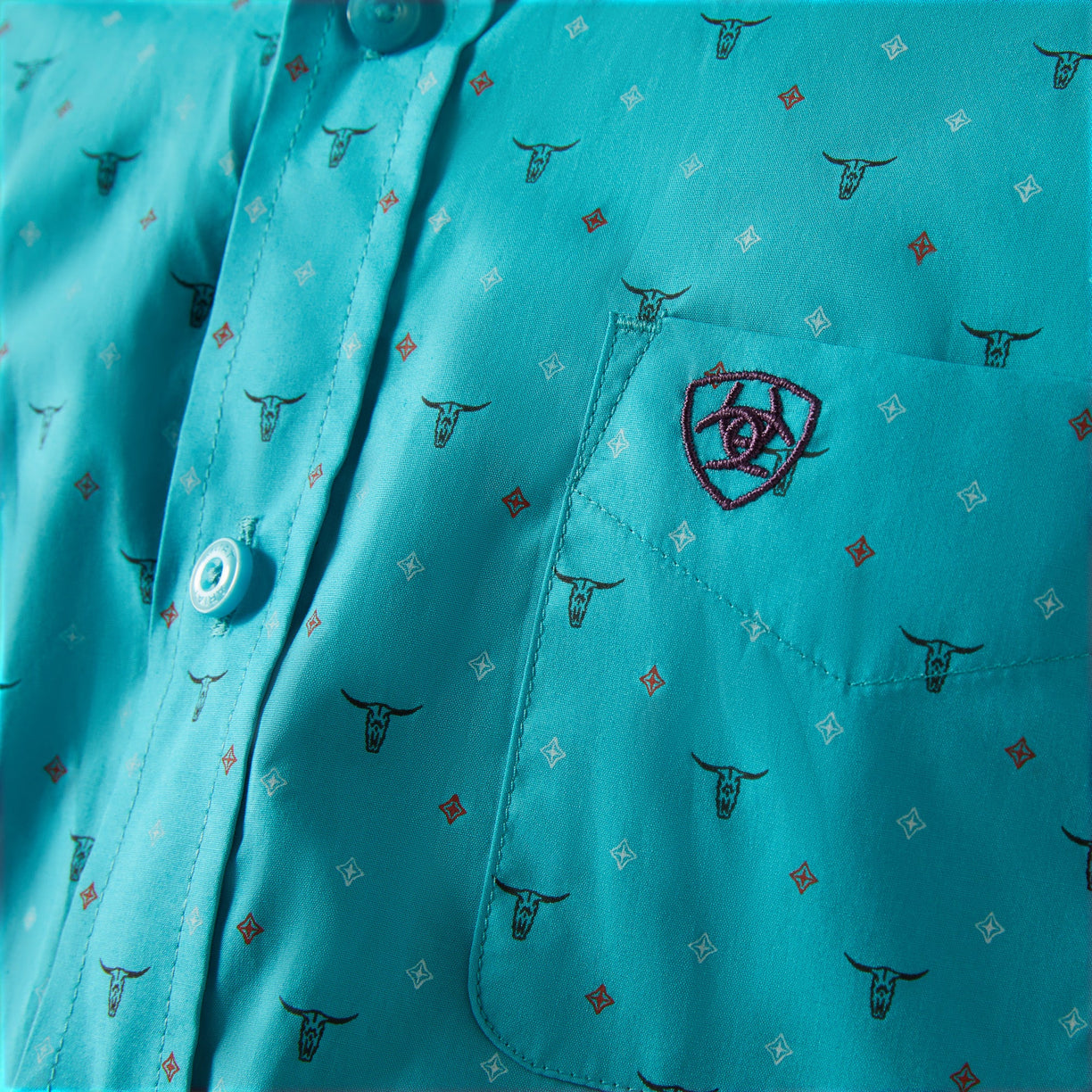 Close-up of a turquoise shirt with bull head pattern and embroidered logo.